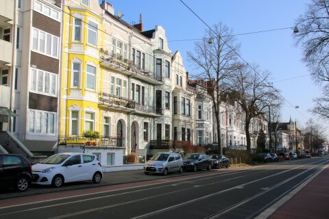 Mehrere Altbremer Häuser stehen aneinander gereiht. Davor parken Autos und die Sonne scheint.