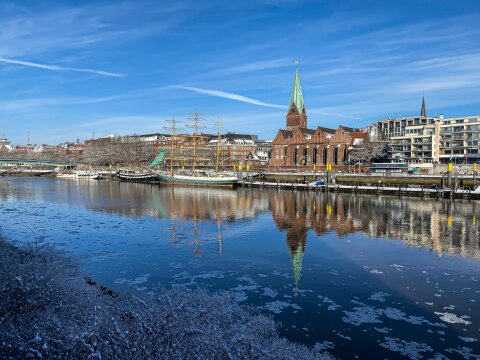 An der Schlachte stehen drei Boote. Es schwimmen Eisstücke auf der Weser und in den Bäumen hängt Schnee. Der Himmel ist strahlendblau.