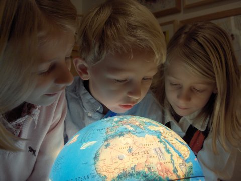 Drei Schüler betrachten einen leuchtenden Globus