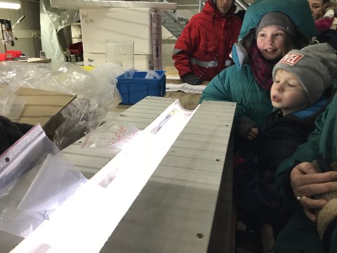 Zwei Kinder in Winterkleidung betrachten mit einer Personengruppe eine leuchtende Röhre mit Eisproben