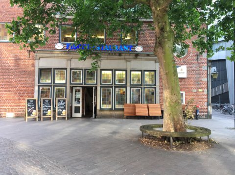 Eine Außenaufnahme des Fischrestaurants namens Knurrhahn. Vor dem roten Backsteingebäude steht ein großer Baum.