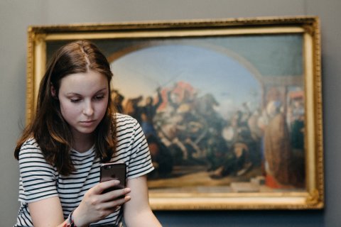 Ein Mädchen mit einem Smartphone in der Hand vor einem Gemälde