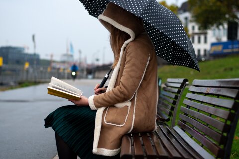 Eine Frau sitzt auf einer Bank am Osterdeich und liest.