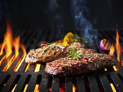 Gegrilltes Steak auf einem Rost, im Hintergrund Feuer.