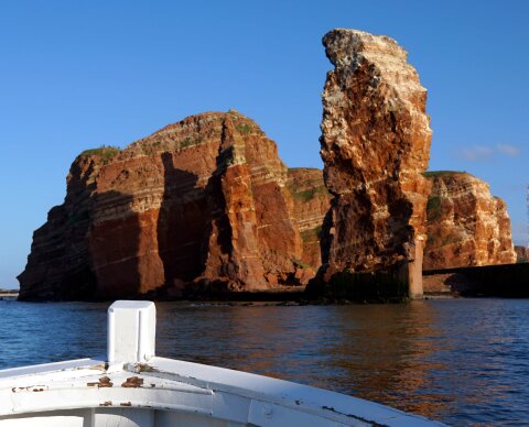 Der Blick geht von einem kleinen weißen Boot auf die Steilküste Helgolands.