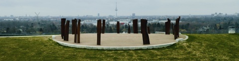 Der Blick von oben auf die Aussichtsplattform Metalhenge: Mehrere Metall-Stelen stehen in einem Kreis auf einer runden Platte. Im Hintergrund ist der Panoramablick auf Bremen zu erkennen.