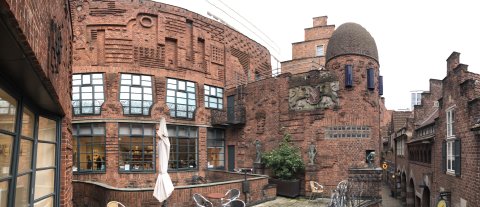 Die rotbraune Außenfassade der Museen Böttcherstraße mit Terrasse und Kuppel. Auf der rechten Bildseite ist ein kleiner Teil der Gasse "Böttcherstraße" zu erkennen.