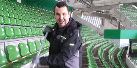 Ein Mann reinigt die Sitze eines Fußballstadions.