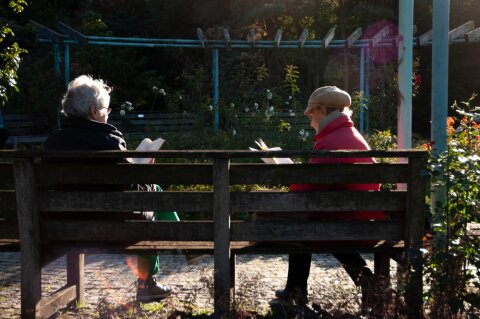 Zwei alte Frauen sitzen auf einer Bank im Park und lesen.