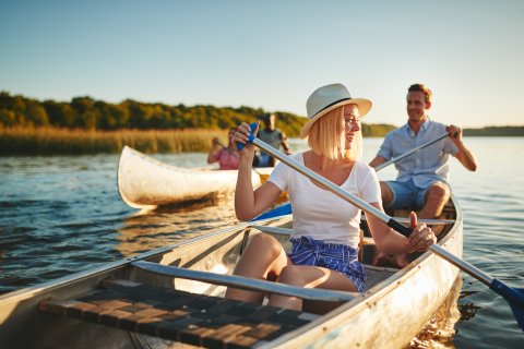 Zwei Ruderboote auf einem Fluss, jeweils gesteuert von einer Frau und einem Mann.