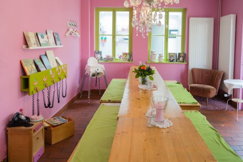Ein Raum im Radieschen mit rosafarbenen Wänden, einem langen Tisch und Kinderspielzeug an der Seite.
