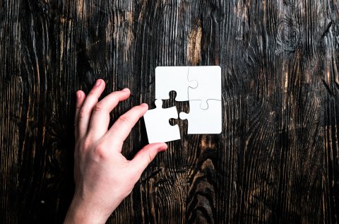 Eine Hand ergänzt ein letztes Puzzleteil zu einem Puzzle, das ein Rechteck formt.