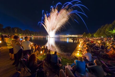 Menschen sitzen um den Hollersee und beobachten das Feuerwerk über dem See