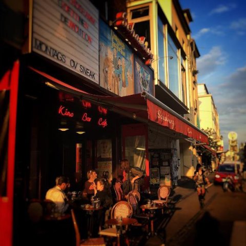 Die Schauburg mit Menschen an Tischen vor der Tür in der Abendsonne