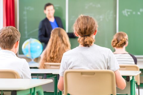 a teacher stands at a blackboard in front of a school class 