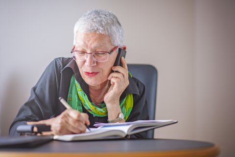 Eine Seniorin schreibt etwas in eine Notizbuch, während sie telefoniert.