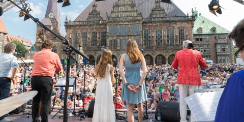 Auf der Bühne vorm Domshof stehen mehrere Musiker*innen und singen. 