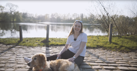 Eine junge Frau sitzt mit ihrem Hund vor einem See.