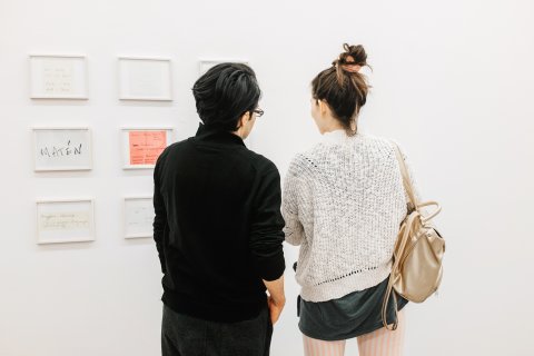Zwei Menschen stehen mit dem Rücken zur Kamera und schauen sich Bilder an der Wand an.