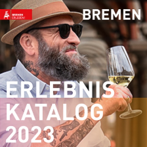 Zu sehen ist ein Mann mit einem Glas Weißwein in der Hand. Er trägt eine Sonnenbrille. Auf dem Bild ist der Schriftzug "Erlebnis Katalog 2023" zu lesen. 