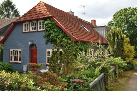 Ein blaues Wohnhaus mit rot-braunen Ziegeln, umgeben von Garten.