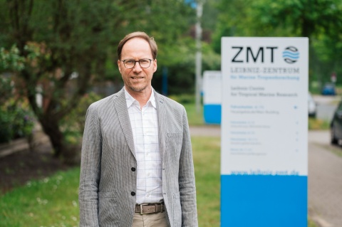 Mann mit Brille und grauem Anzug vor dem ZMT-Schild