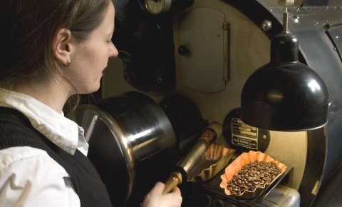 Eine Frau nimmt Kaffeebohnen aus einer großen Maschine.