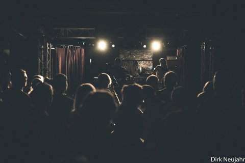 Die Bühne der Zollkantine ist in dunkles Licht gehüllt. Auf der Bühne stehen die drei Musiker der Band Rote Planeten.