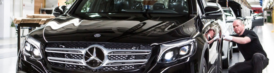 Ein Mann kniet neben einem neu produzierten dunklen Mercedes.