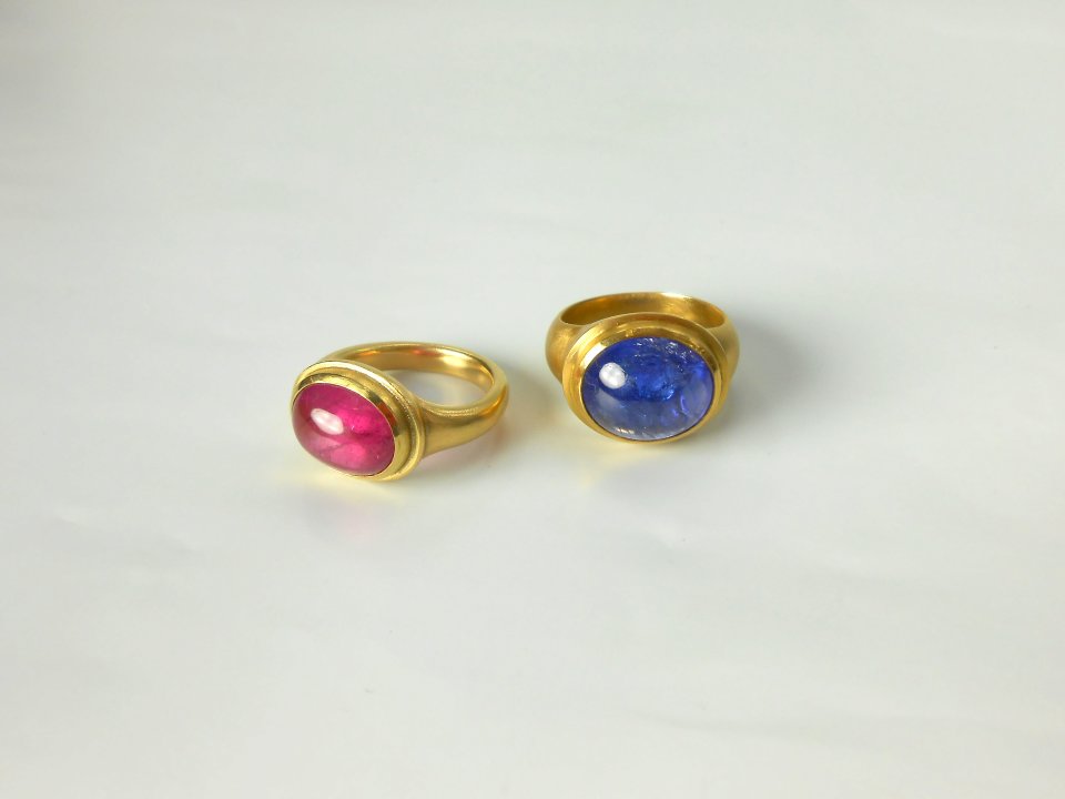 Zwei große Goldringe mit Steinen. Ein Ring hat einen pinken Stein und der andere einen blauen Stein.