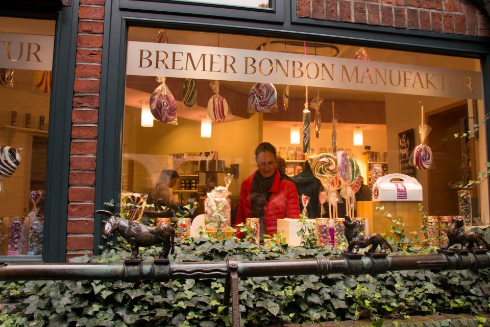 Ein Foto von Außen in das Fenster der Bonbon Manufaktur Böttcherstraße. Leckere Bonbons und große Lollis sind in allen Farben zu sehen.
