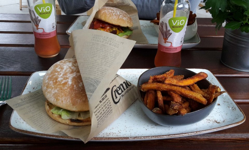 Zwei Menus mit Burgern, Süßkartoffelpommes und Rhabarberschorle auf dunklem Holztisch.