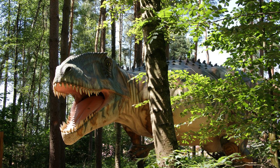 Lebensgroßes Modell eines Giganotosaurus zwischen Bäumen.