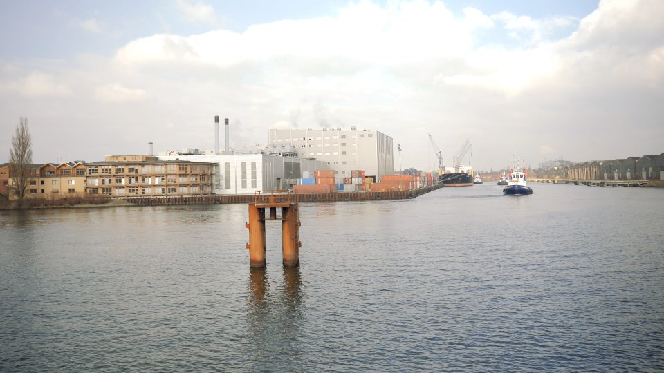 Zu sehen ist das Wasser der Weser. Auf der gegenüberliegenden Seite befinden sich Gebäude in Ufernähe. Rechts legt ein Schiff an, drei kleinere Boote liegen in der Nähe des Schiffs auf dem Wasser.