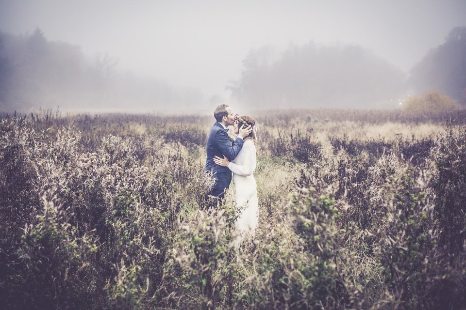 Ein Brautpaar kuesst sich in einem Feld