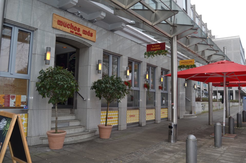Das spanische Restaurant "Mucho Más" von außen. Große rote Sonnenschirme stehen vor der Tür "Am Wall 136".