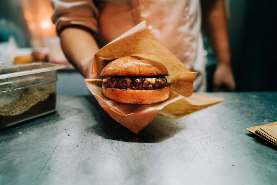 Ein Burger wird von einer Person in die Kamera gehalten. 