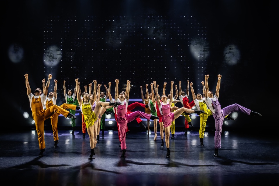 Mehrere Ballett-Tänzer*innen stehen in bunten Kostümen auf einer Bühne.