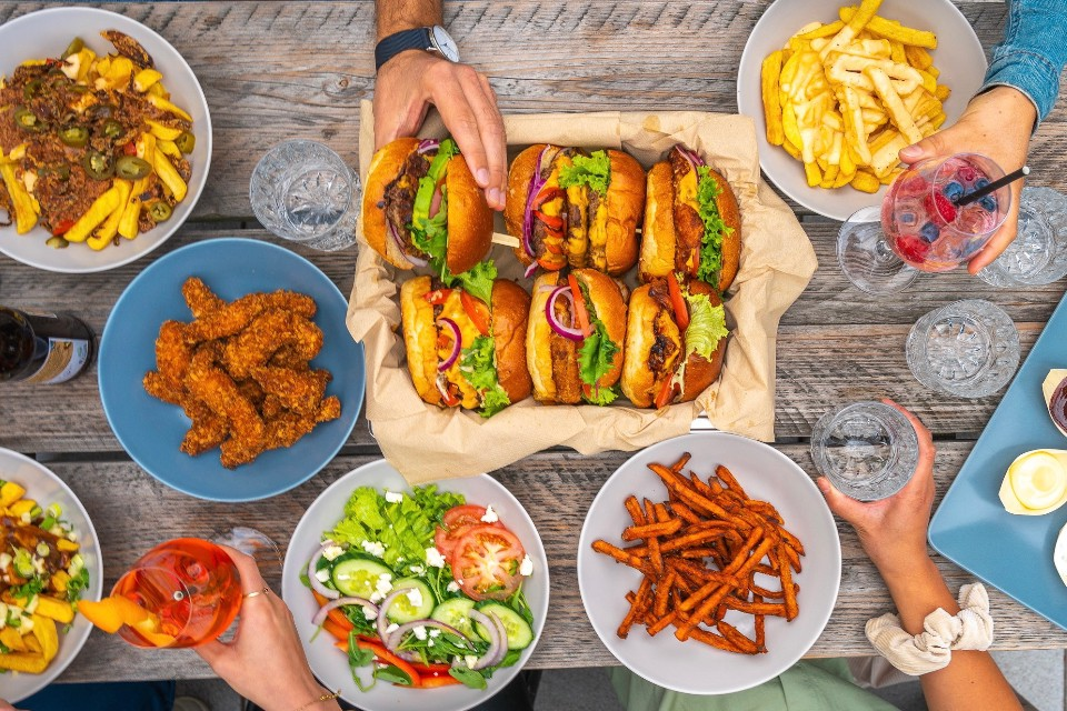 Ein Tisch voll mit Burgern und Pommes, am Bildrand einige Hände, die nach dem Essen greifen