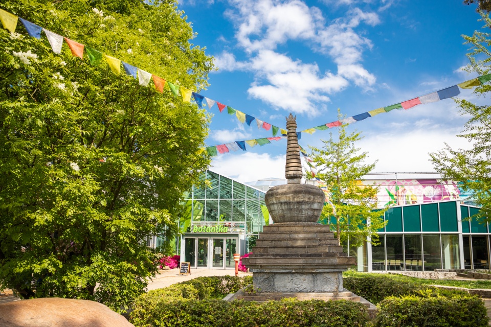 Ein buddhistisches Monument (Stupa), an dem Gebetsfahnen hängen, steht vor der botanika.