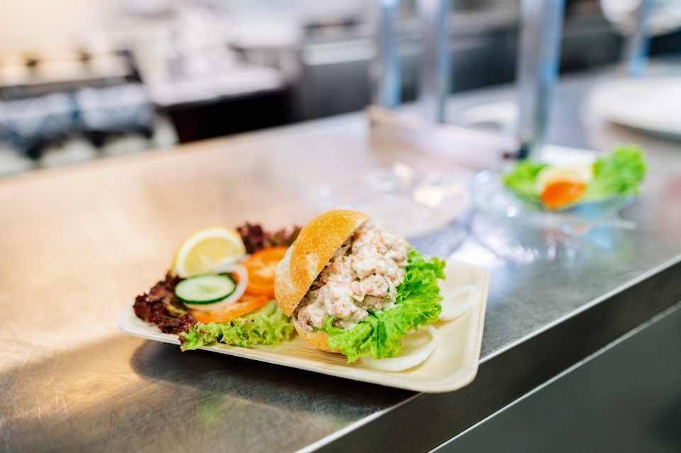 Ein Krabbenbrötchen garniert mit Salat auf einem Teller.