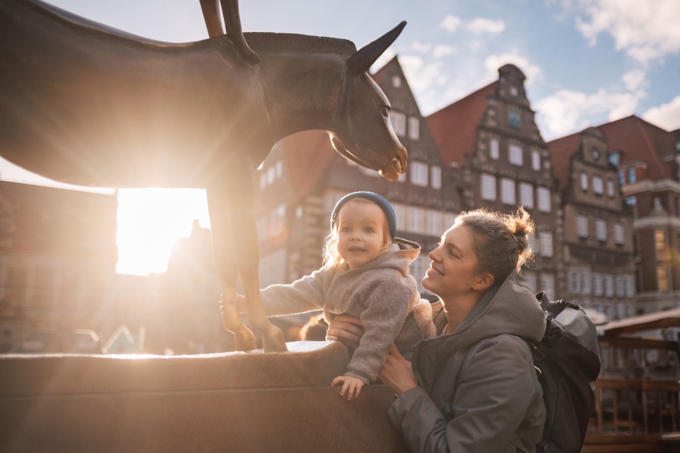 Das Foto zeigt eine Mutter und ihr Kind, wie sie den Esel der Bremer Stadtmusikanten anfassen.