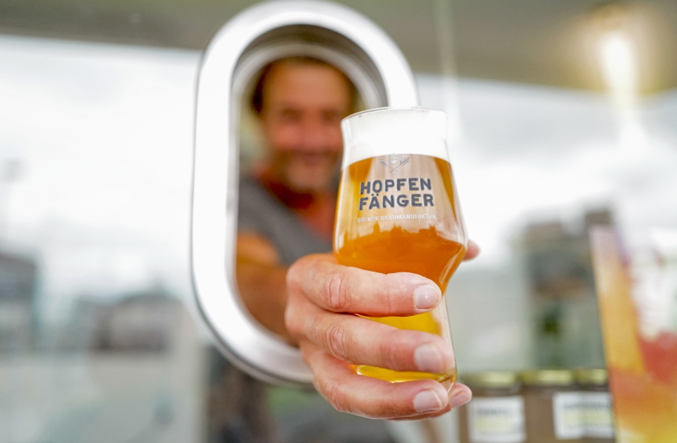 Ein Mann hält ein Bierglas durch ein Fenster. 