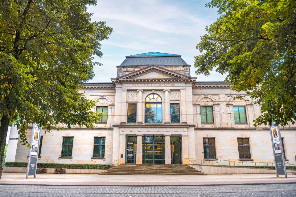 Ein Bild des klassizistischen Gebäudes der Kunsthalle Bremen, eingerahmt durch grüne Baumkronen, die neben dem Gebäude stehen.