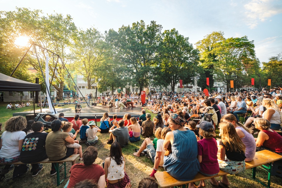 In der grünen Parkanlage "Wallanlagen" sitzen viele Menschen und schauen Artist*innen bei einer Vorführung zu.