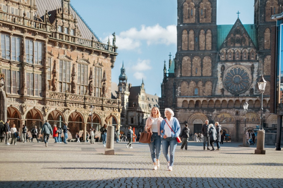 Zwei Damen laufen über einen großen Platz und eine Kirche ist im Hintergrund.