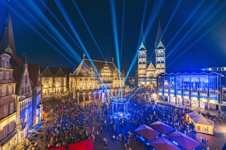 Der historische Bremer Marktplatz bei Nacht. Zahlreiche Leute sind dort und schauen einer Liichtshow zu.