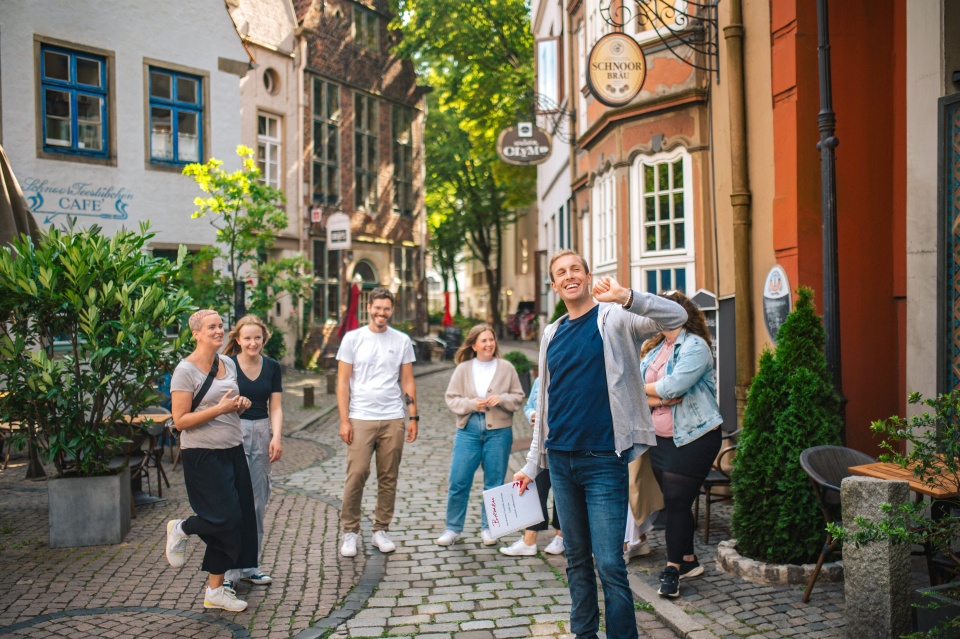 Ein Mann führt eine Gruppe durch das Schnoorviertel vorbei an kleinen Häusern in einer schmalen Gasse.