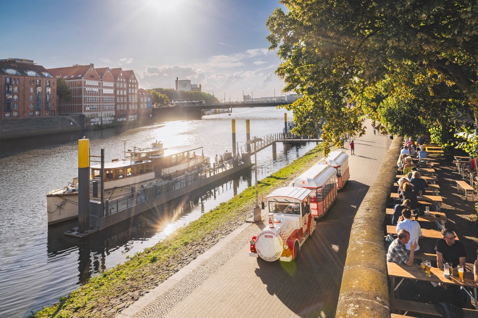 Eine kleine Bummelbahn fährt an einer Promenade entlang.