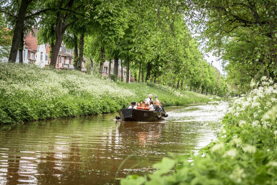 Ein Torfkahn fährt auf einem kleinen Fluss, die Umgebung ist grün.